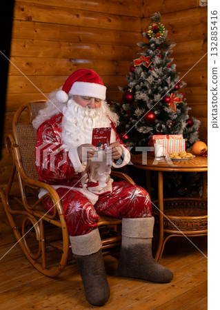 Santa Claus reading a book in a chair, with a Christmas tree behind him 132885416