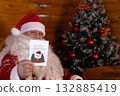 Santa holding Christmas card with tree backdrop 132885419