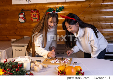 girls making Christmas cookies: rolling dough, the other cutting shapes. girls making Christmas cookies: rolling dough, the other cutting shapes. 132885421