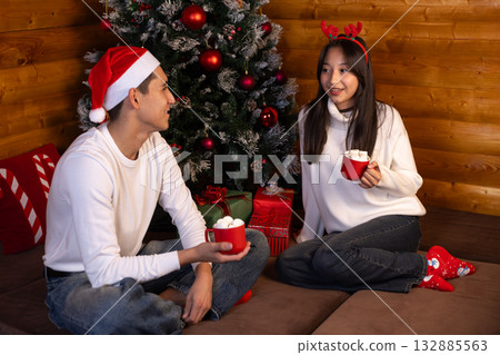 couple is sitting by a Christmas tree,enjoying hot chocolate on a cozy Christmas couple is sitting by a Christmas tree,enjoying hot chocolate on a cozy Christmas 132885563