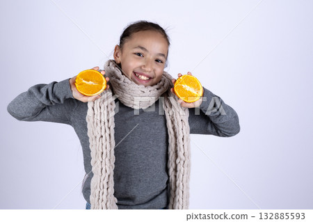 A smiling child is holding two orange halves to their ears 132885593