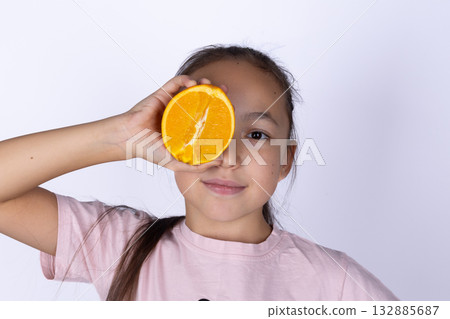 A girl playfully holds a festive orange,a traditional Christmas stocking stuffer A girl playfully holds a festive orange,a traditional Christmas stocking stuffer 132885687