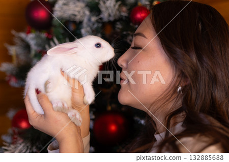 A woman kisses a white rabbit by a Christmas tree A woman kisses a white rabbit by a Christmas tree 132885688