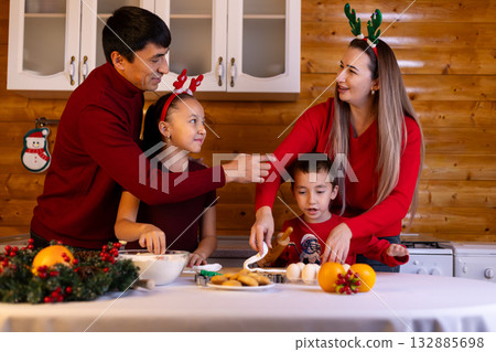 Family joyfully preparing Christmas cookies together with colorful decorations. 132885698