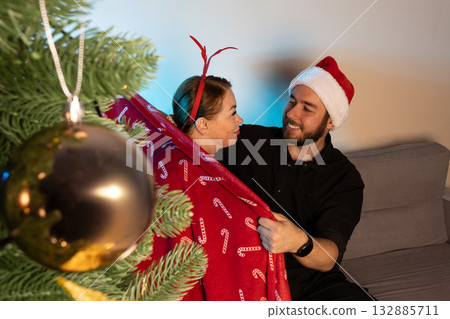 A man in a Santa hat is playfully wrapping a woman in a festive blanket A man in a Santa hat is playfully wrapping a woman in a festive blanket 132885711
