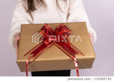 Womanis holding a Christmas gift wrapped in golden paper with a red bow 132885730