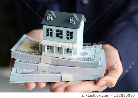 Businessman holding a house model on top of stacks of money, representation of real estate investment, home loan, selling, renting, insurance. 132886050