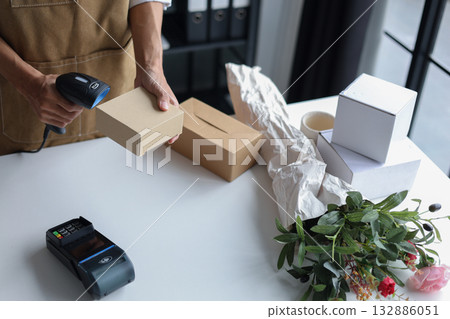 A person using a barcode scanner to scan a small cardboard box in a retail shop for inventory management or preparing an order for customer. 132886051