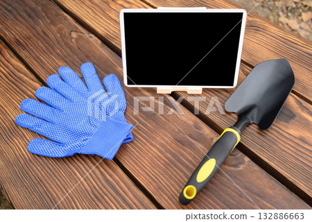 blue glove, a tablet and a trowel are lying on a wooden table for garden and vegetable garden blue glove, a tablet and a trowel are lying on a wooden table for garden and vegetable garden 132886663