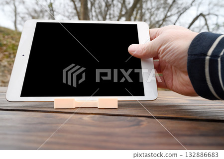 a hand holds a white tablet horizontally over a wooden table close-up 132886683