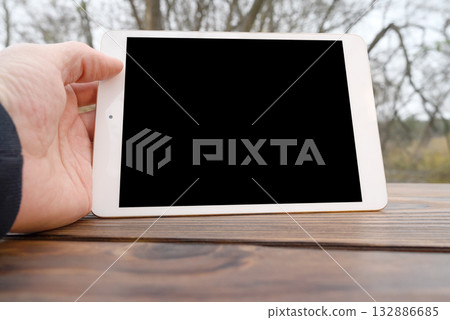 a person holds a white tablet horizontally over a wooden table close-up a person holds a white tablet horizontally over a wooden table close-up 132886685