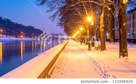 夜晚,輕柔的雪花和燈光倒映在靜謐的河畔長廊上。 夜晚,輕柔的雪花和燈光倒映在靜謐的河畔長廊上。 132886826