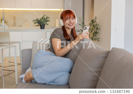 Young woman with wireless headphones listens to music from smartphone relax calm rest gentle smile Young woman with wireless headphones listens to music from smartphone relax calm rest gentle smile 132887190
