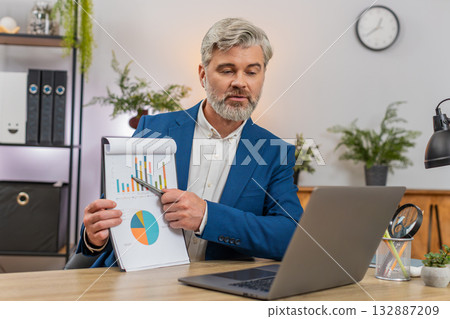 Middle-aged businessman shows chart via laptop remote call big drop proposes recovery plan gestures Middle-aged businessman shows chart via laptop remote call big drop proposes recovery plan gestures 132887209