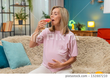 Pregnant woman eating donut with appetite smiling enjoying sugary treat during pregnancy craving joy 132887210