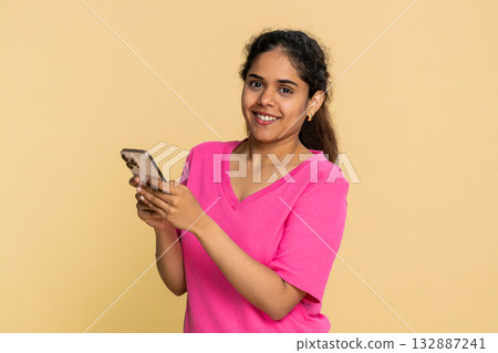 Indian woman smiling holding smartphone, actively texting message, cheerfully engaging online chat 132887241