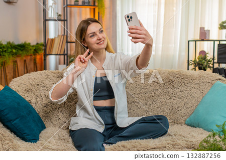 Adult woman taking cheerful selfie on smartphone at home smiling brightly posing with playful energy 132887256