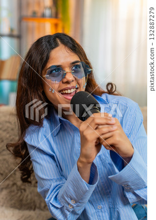 Indian woman singing into microphone with energetic smile, imagining life as pop superstar at home Indian woman singing into microphone with energetic smile, imagining life as pop superstar at home 132887279
