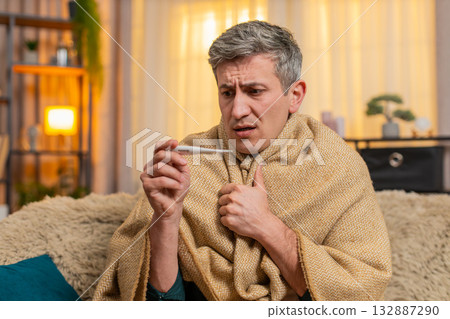 Young man checks body temperature with thermometer looks worried about possible illness and fever 132887290
