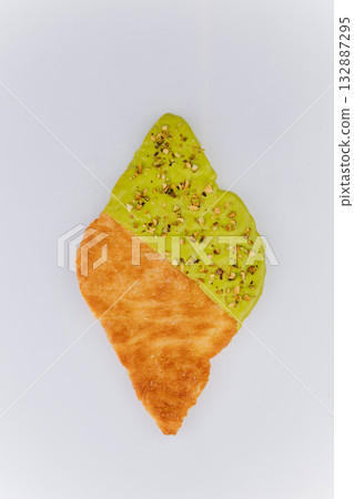 Flaky croissant dipped in green pistachio glaze and crushed nuts on white background Flaky croissant dipped in green pistachio glaze and crushed nuts on white background 132887295