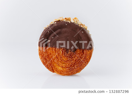 Round croissant pastry coated with chocolate glaze and crushed hazelnuts on white background 132887296