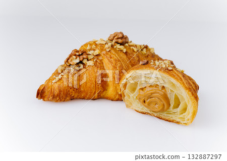 Flaky croissant filled with caramel cream and topped with walnuts on white background Flaky croissant filled with caramel cream and topped with walnuts on white background 132887297
