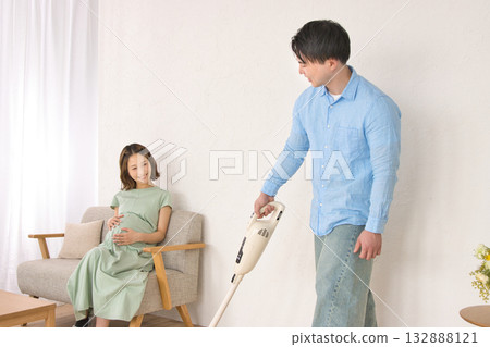 一位年輕男子一邊愉快地吸塵，一邊和孕婦聊天。 132888121
