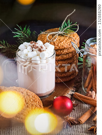 A Christmas photo with marshmallows in a mug and cinnamon sticks, as well as Christmas cookies and fir branches, as well as star anise fir cones and red Christmas tree decorations nearby A Christmas photo with marshmallows in a mug and cinnamon sticks, as well as Christmas cookies and fir branches, as well as star anise fir cones and red Christmas tree decorations nearby 132888260