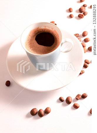 Coffee in a blue cup sits on a white table with coffee beans scattered nearby. 132888295