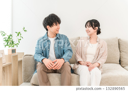 一對年輕的亞洲夫婦坐在家裡客廳的沙發上 132890565