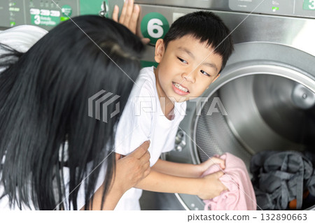 A young boy helps an adult load laundry into a washing machine, highlighting teamwork and shared household chores.. A young boy helps an adult load laundry into a washing machine, highlighting teamwork and shared household chores.. 132890663