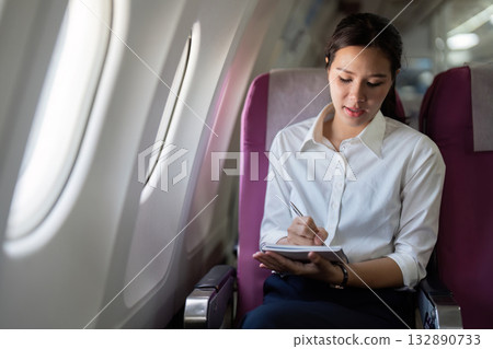 Note-taking on Airplane. Businesswoman writing in notebook during flight. Note-taking on Airplane. Businesswoman writing in notebook during flight. 132890733