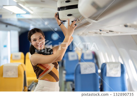 Air Travel Experience. Young woman smiling while placing luggage in overhead compartment on airplane. 132890735