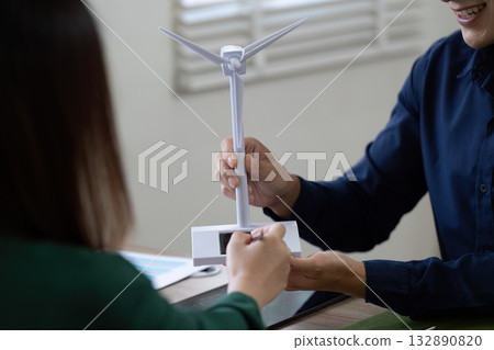 Sustainable Energy Presentation. Professionals showcasing renewable energy solutions with wind turbine model. 132890820