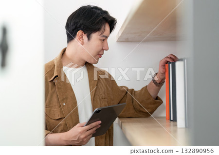 Student Searching for Resources. Young man exploring bookshelf with tablet. Student Searching for Resources. Young man exploring bookshelf with tablet. 132890956