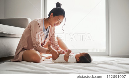 A young Japanese mother smiles as she looks at her baby in a minimalist living room 132891007
