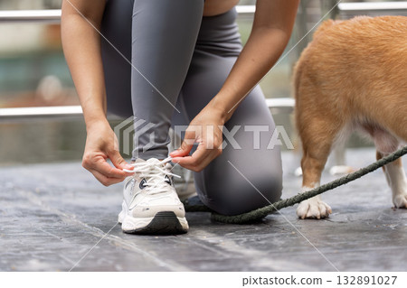 Wellness and Fitness. Woman preparing for a walk with her dog, tying shoelaces outdoors. 132891027