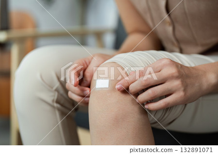 First Aid Care. Woman applying a bandage to her knee injury at home. 132891071