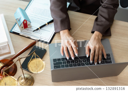Legal Research and Documentation. A lawyer typing on a laptop while reviewing legal documents. 132891316