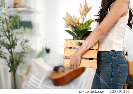 Moving Home with Style. A woman carrying a wooden crate filled with plants and decor in a modern living space. Moving Home with Style. A woman carrying a wooden crate filled with plants and decor in a modern living space. 132891351