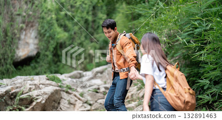 Couple Hiking Together. Young man helping woman navigate rocky trail in lush nature. Couple Hiking Together. Young man helping woman navigate rocky trail in lush nature. 132891463