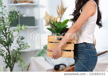 Moving Home with Plants. A woman carries a wooden crate filled with decorative plants. 132891531