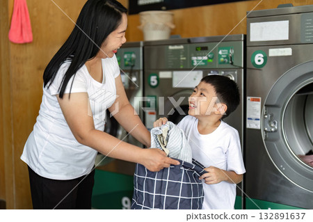 A joyful interaction as a mother hands laundry to her son, promoting teamwork and connection in household tasks.. A joyful interaction as a mother hands laundry to her son, promoting teamwork and connection in household tasks.. 132891637