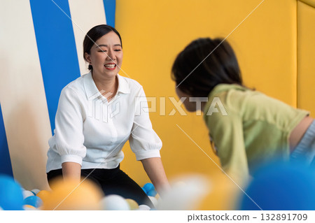 Mother and Child Bonding. Smiling woman engaging with child in colorful ball pit. Mother and Child Bonding. Smiling woman engaging with child in colorful ball pit. 132891709