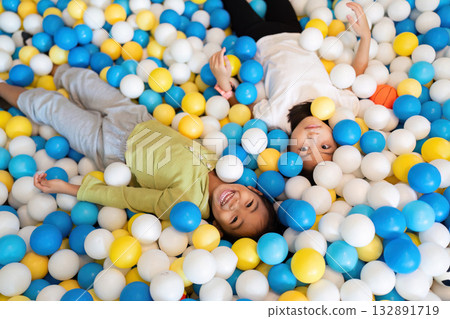 Joyful Playtime in Ball Pit. Two children lying together in colorful ball pit, enjoying carefree moments. Joyful Playtime in Ball Pit. Two children lying together in colorful ball pit, enjoying carefree moments. 132891719