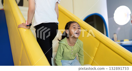 Playful Sliding Fun. Child laughing while climbing up slide, enjoying playful moments in a vibrant environment. 132891733