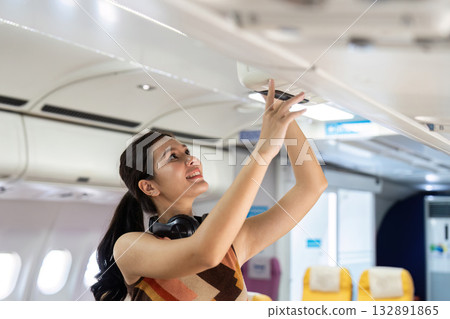 Travel Convenience. Young woman adjusting overhead compartment on airplane. Travel Convenience. Young woman adjusting overhead compartment on airplane. 132891865