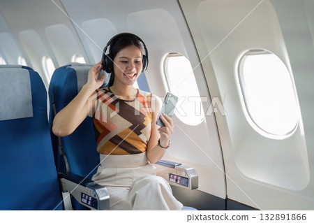 Happy Traveler Listening to Music on Airplane. Young woman enjoying her flight experience with headphones. 132891866