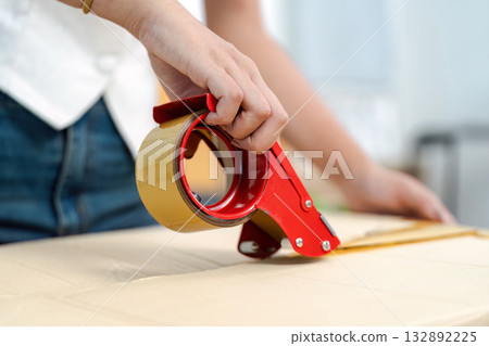 Packing Supplies. Close-up of a hand using a tape dispenser for moving. Packing Supplies. Close-up of a hand using a tape dispenser for moving. 132892225