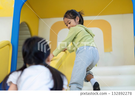 Children Playing in Indoor Playground. A young girl climbing stairs in a colorful play area. 132892278